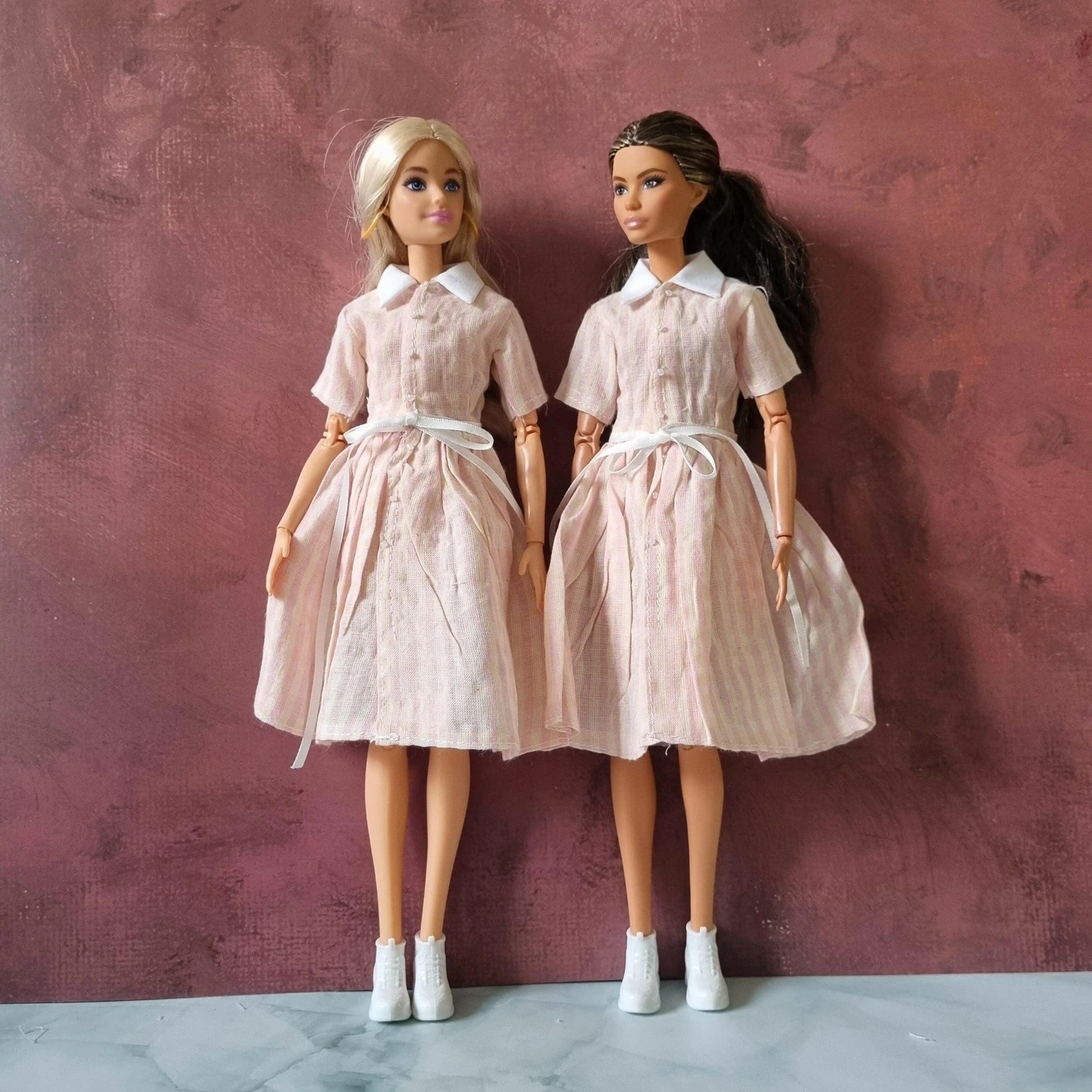 Two Barbie dolls wearing pink striped retro shirt dresses with collars and ties
