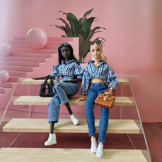 Two Barbie dolls modeling matching blue gingham crop tops and jeans outfits with handbags.