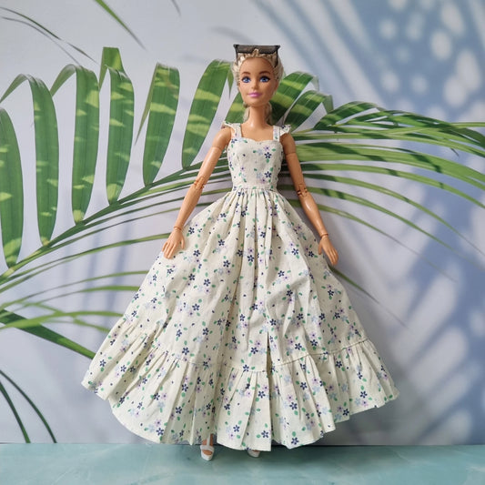 1/6 scale fashion doll wearing a handmade long floral dress with a ruffled hem against a tropical leaf background.