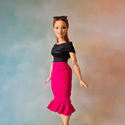 Full body shot of Barbie doll in black top, hot pink mermaid skirt, and black pointed shoes.