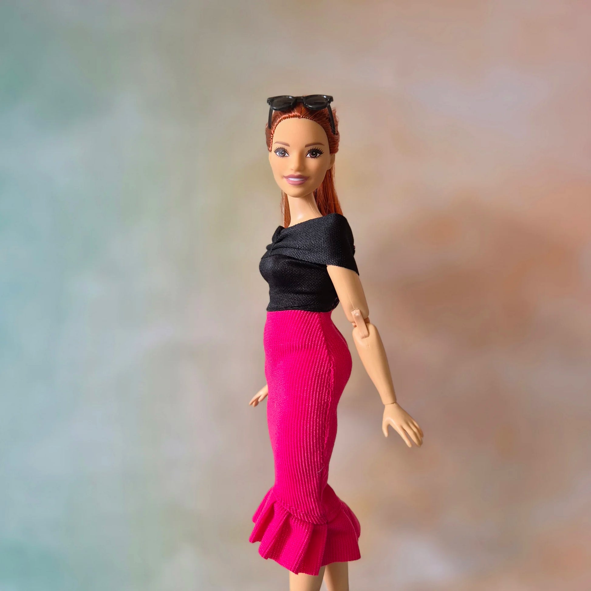 Stylish Barbie doll with red hair in black off-shoulder top and hot pink ruffle hem skirt.