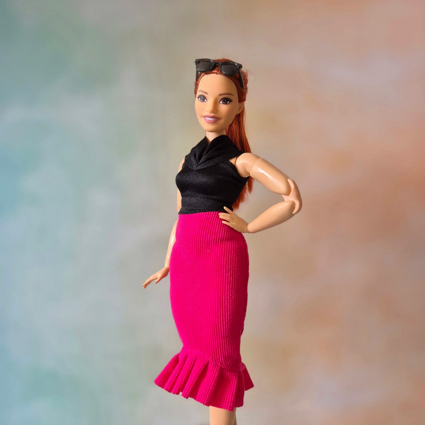 Barbie doll with red hair wearing black top and hot pink ribbed mermaid skirt with ruffle, sunglasses on head.