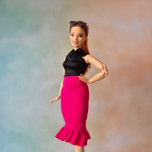 Barbie doll with red hair wearing black top and hot pink ribbed mermaid skirt with ruffle, sunglasses on head.