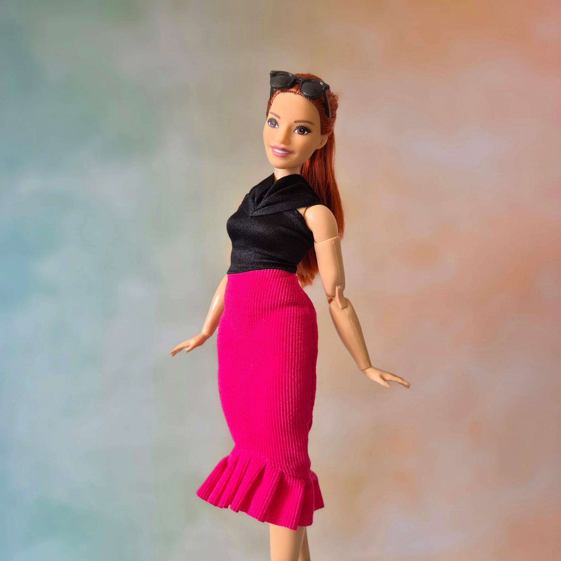 Barbie doll models elegant black top and hot pink mermaid ruffle skirt, side view.