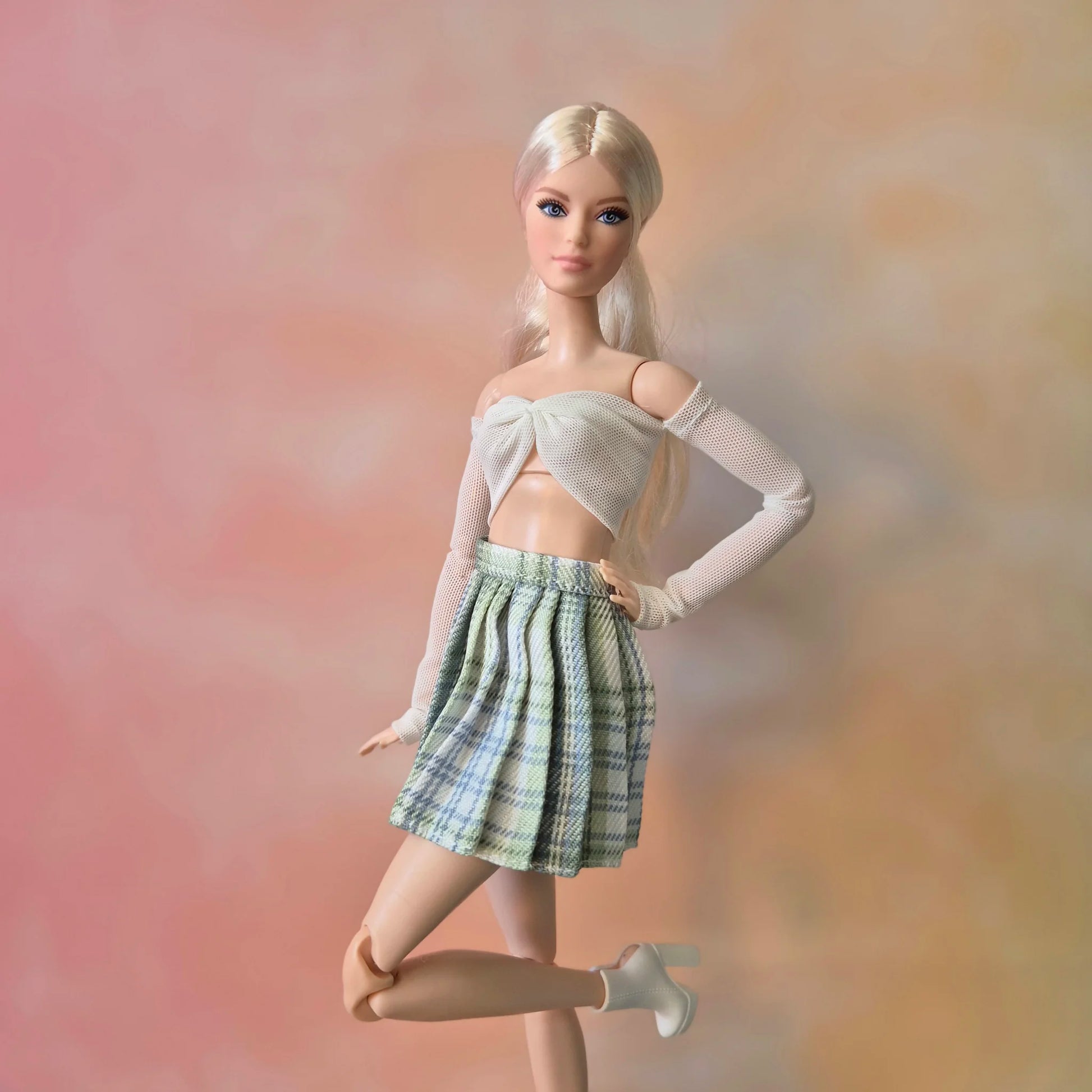 Platinum blonde Barbie doll posing in white tie-front crop top and green plaid skirt.
