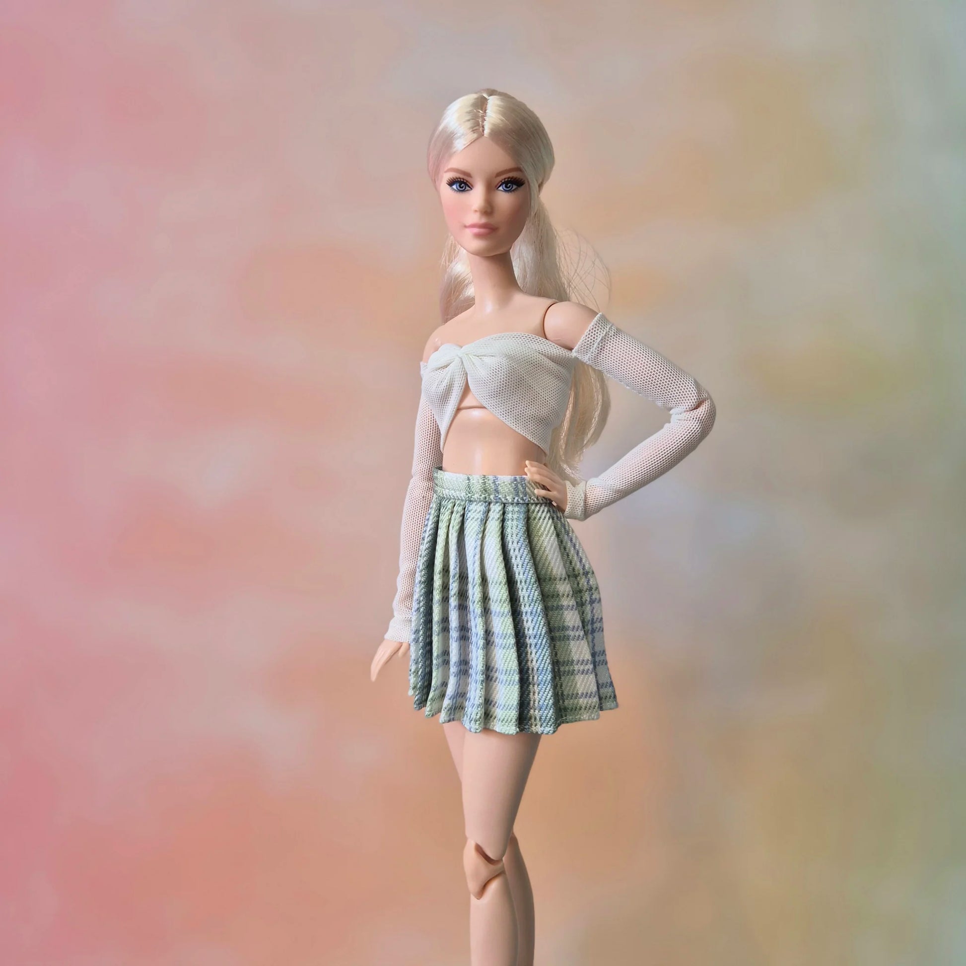 Barbie doll with platinum blonde hair in white mesh sleeve crop top and light green plaid skirt.