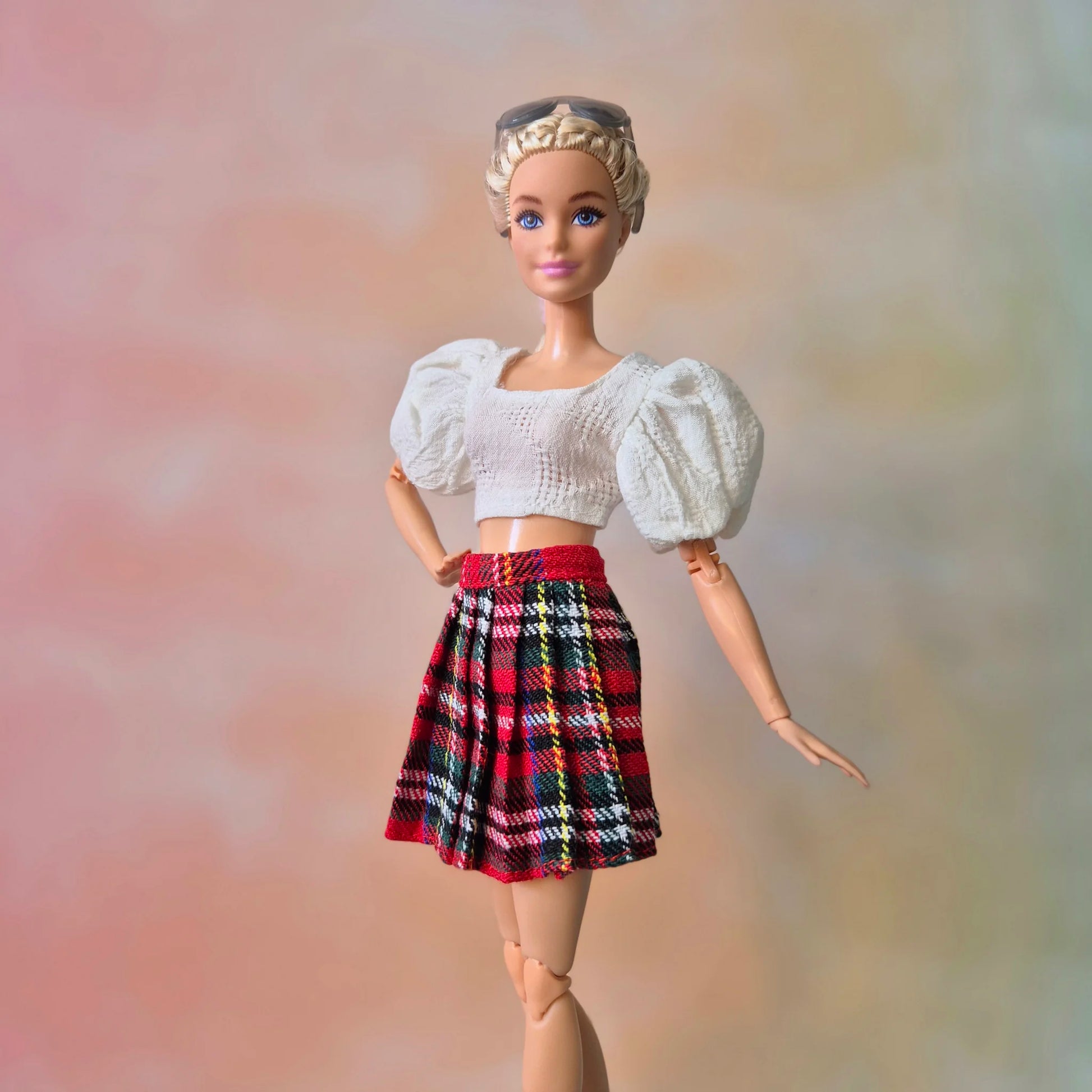 Blonde Barbie doll models white textured puff sleeve top and red plaid pleated skirt.
