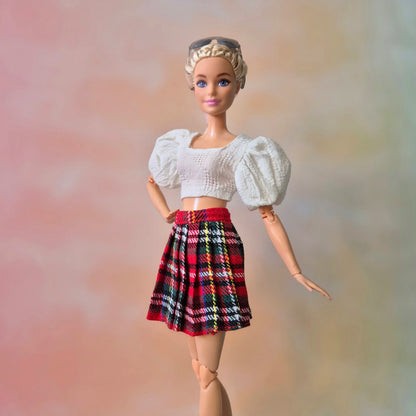 Blonde Barbie doll models white textured puff sleeve top and red plaid pleated skirt.