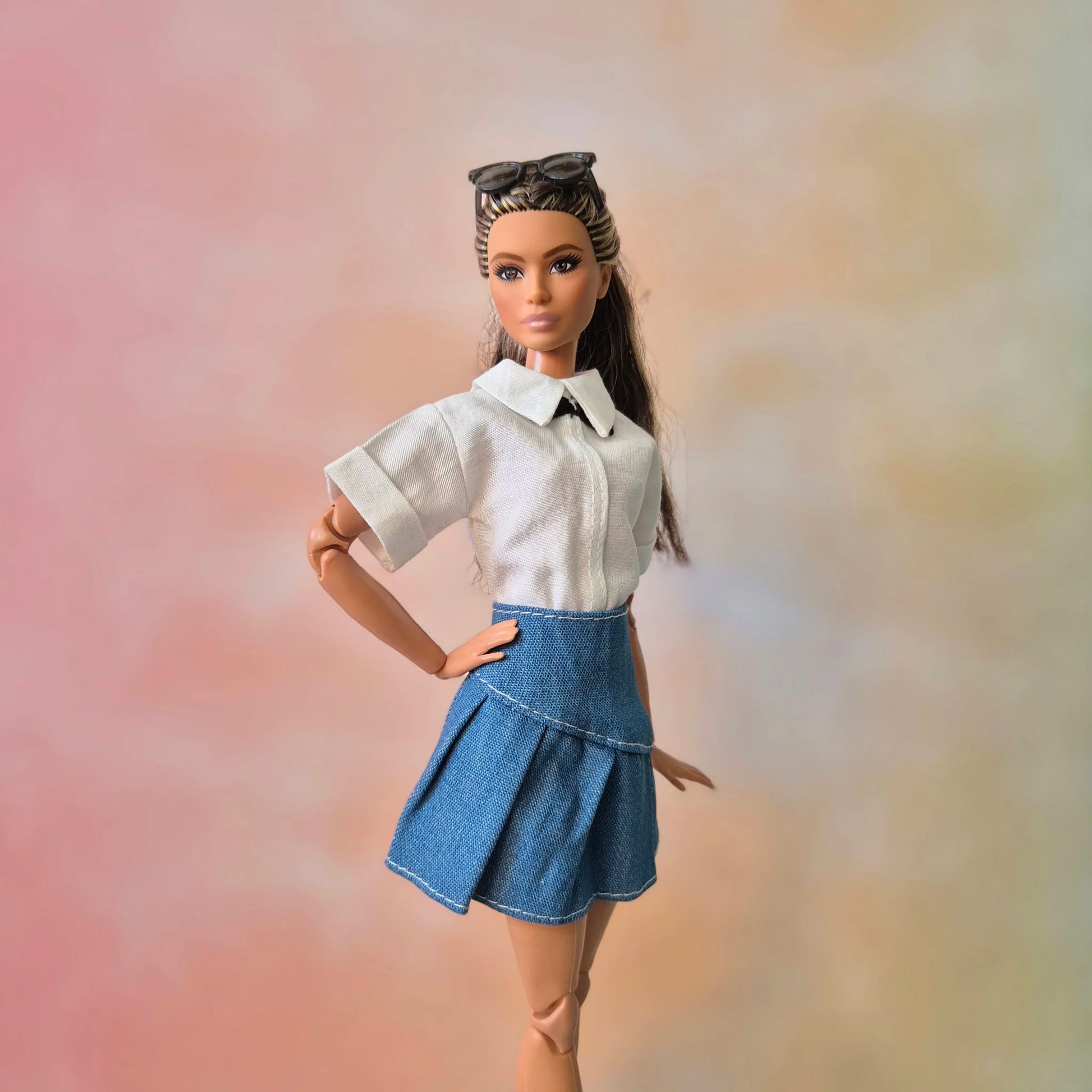 Barbie doll with brown hair wearing white collared crop top and blue denim pleated skirt.