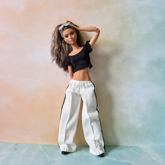 Barbie doll models black crop top and white striped pants outfit, hand on head pose.