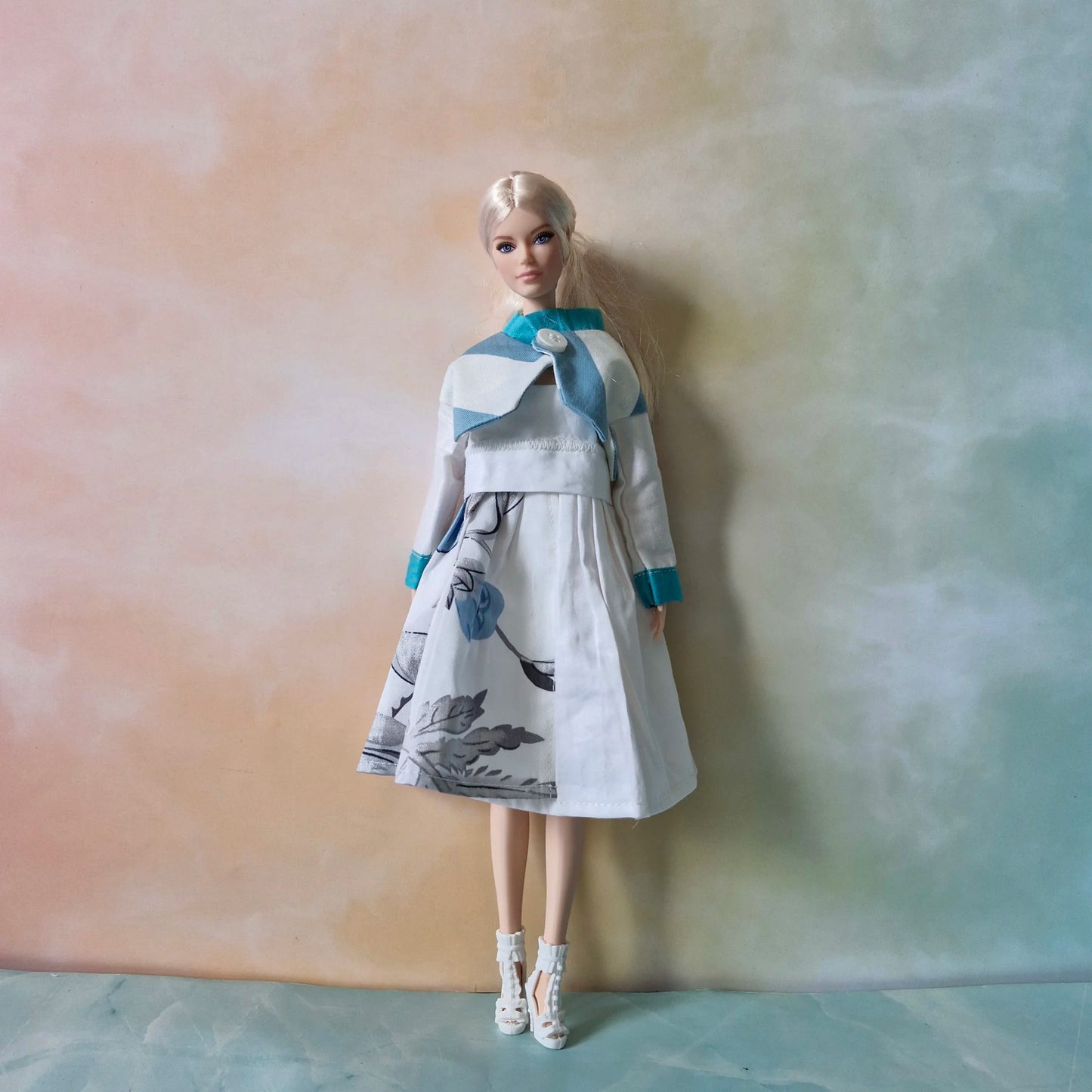 Blonde Barbie doll wearing a white floral print dress and matching white jacket with blue trim