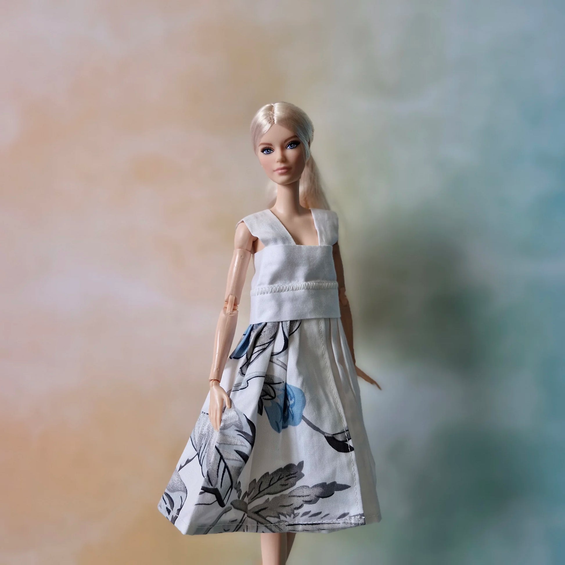 Blonde Barbie doll wearing a white sleeveless dress with a blue and grey floral print skirt.