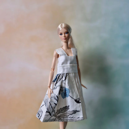 Blonde Barbie doll wearing a white sleeveless dress with a blue and grey floral print skirt.