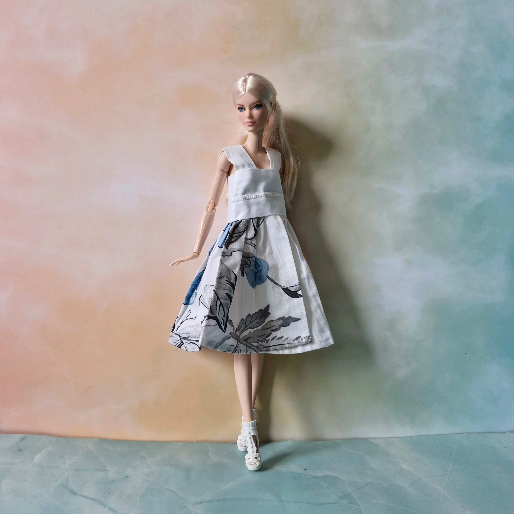 Blonde Barbie doll wearing a white sleeveless dress with a blue and grey floral print skirt.