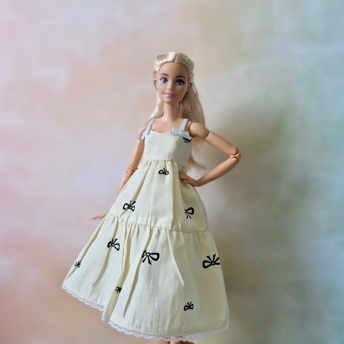 Blonde Barbie doll poses hands on hips wearing cream bow print sundress without t-shirt.
