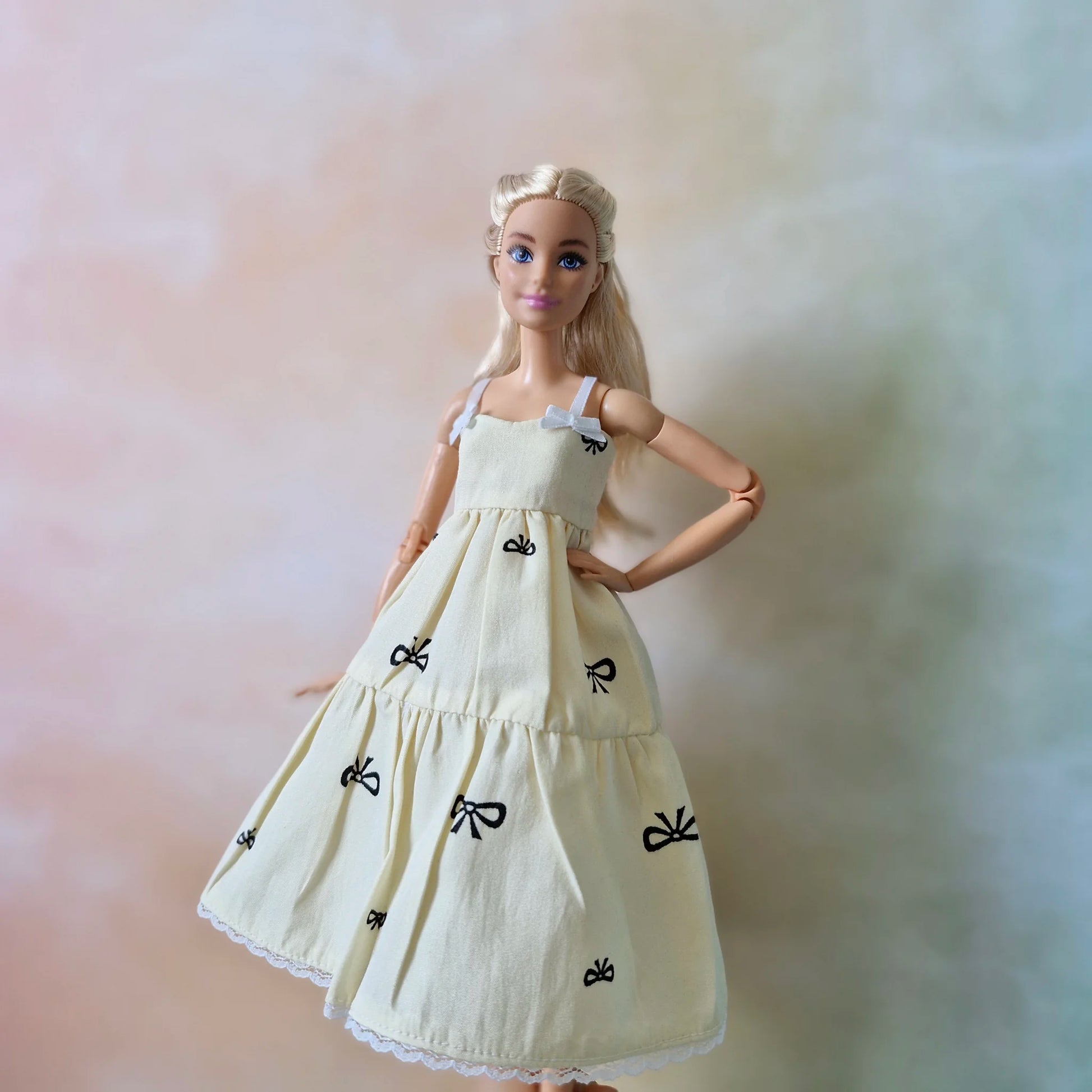 Blonde Barbie doll poses hands on hips wearing cream bow print sundress without t-shirt.