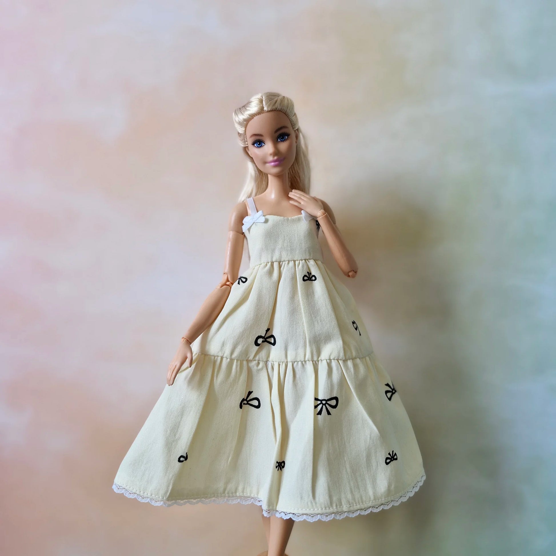 Blonde fashion doll models cream tiered sundress showing strap and bow print detail.