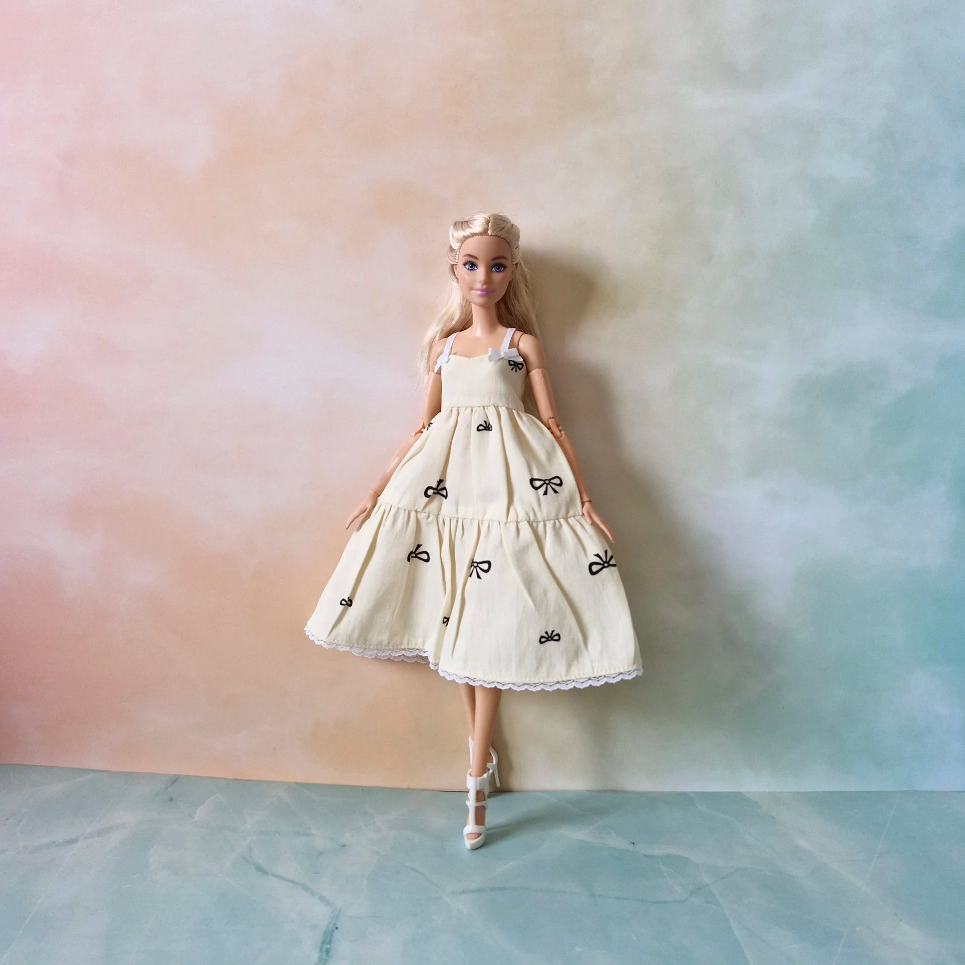 Full length view of blonde Barbie doll modeling cream bow print tiered sundress.