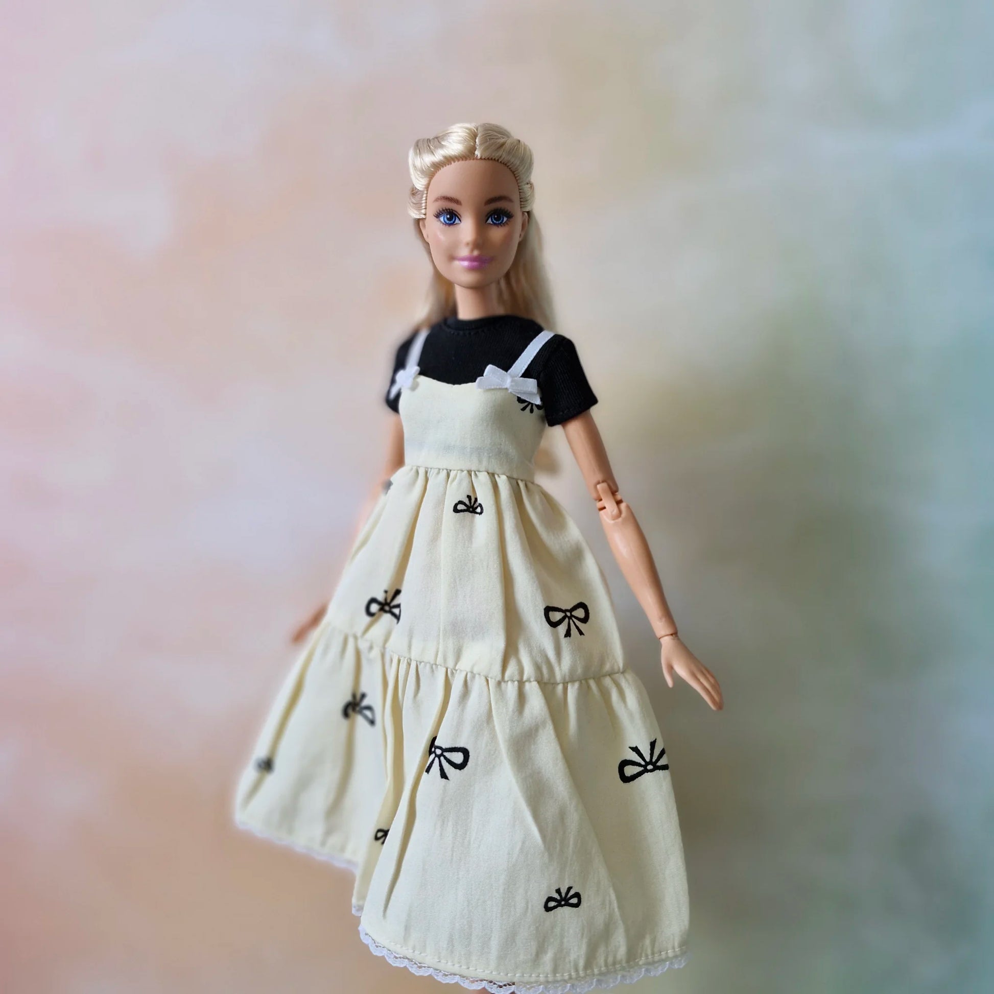 Blonde Barbie doll wearing cream bow print tiered sundress layered over black t-shirt.