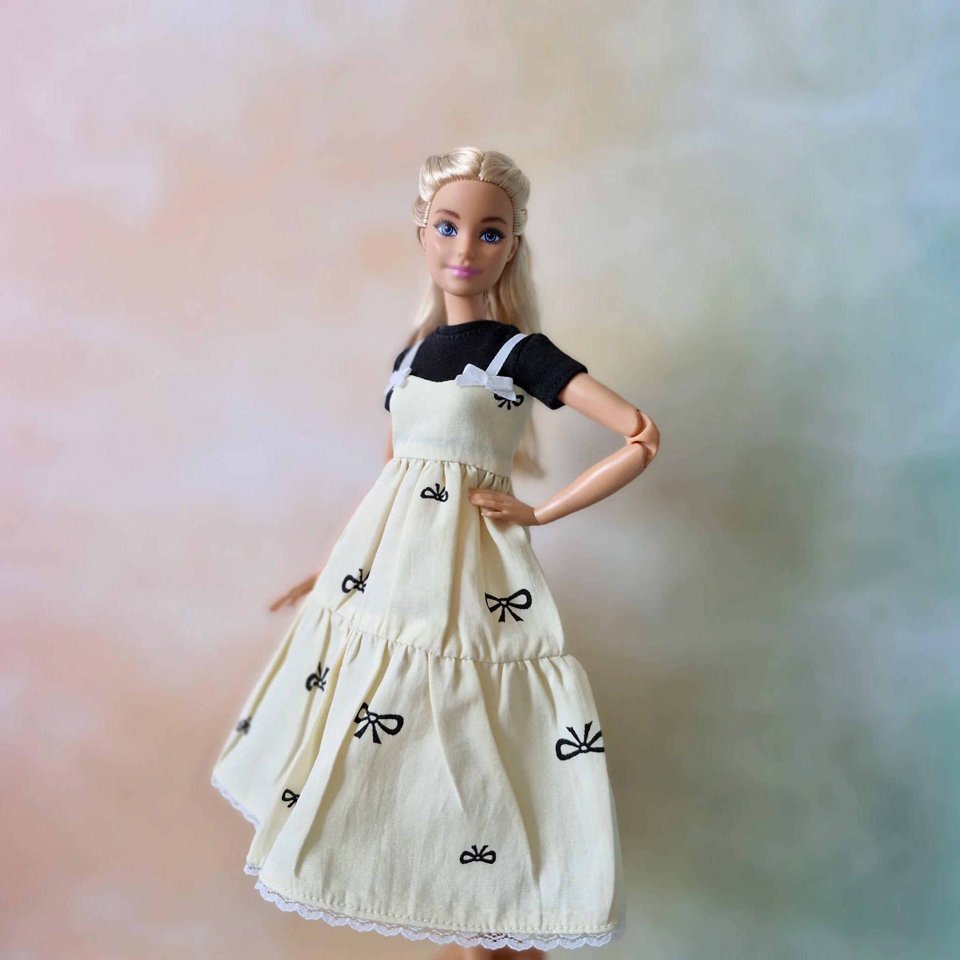 Blonde fashion doll poses in layered outfit: cream bow print sundress and black tee