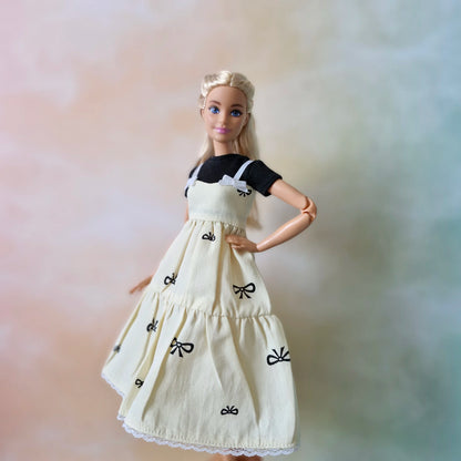 Blonde fashion doll poses in layered outfit: cream bow print sundress and black tee