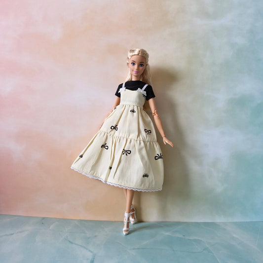 Blonde fashion doll poses in layered outfit: cream bow print sundress and black tee