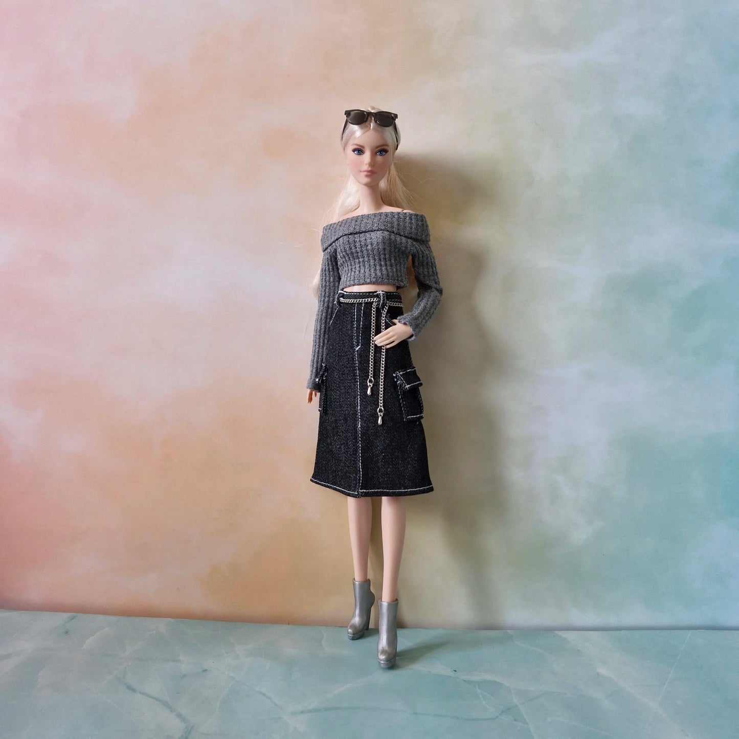 ull length view of fashion doll in grey crop sweater, black cargo skirt with white stitching, and silver boots against a pastel background.