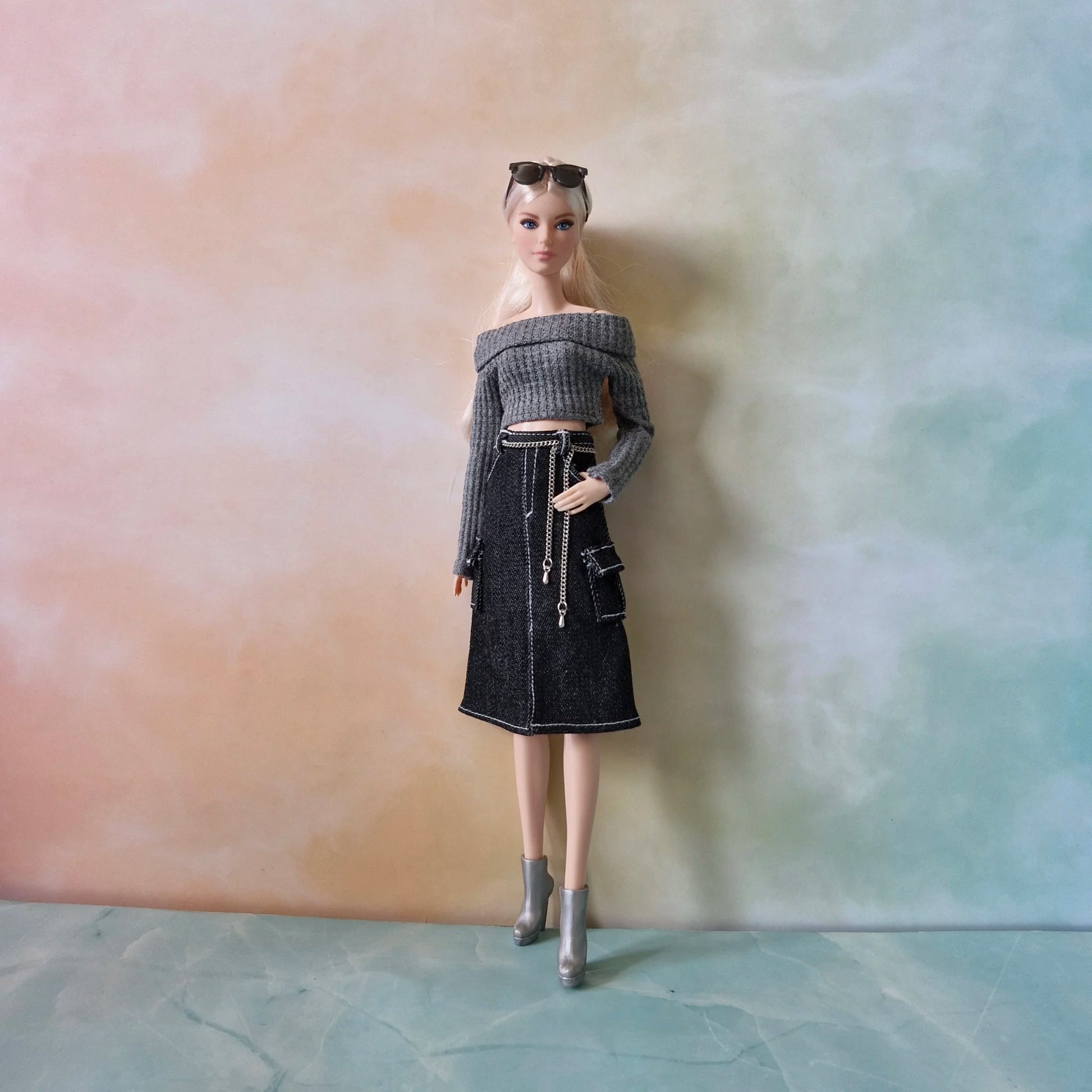 ull length view of fashion doll in grey crop sweater, black cargo skirt with white stitching, and silver boots against a pastel background.