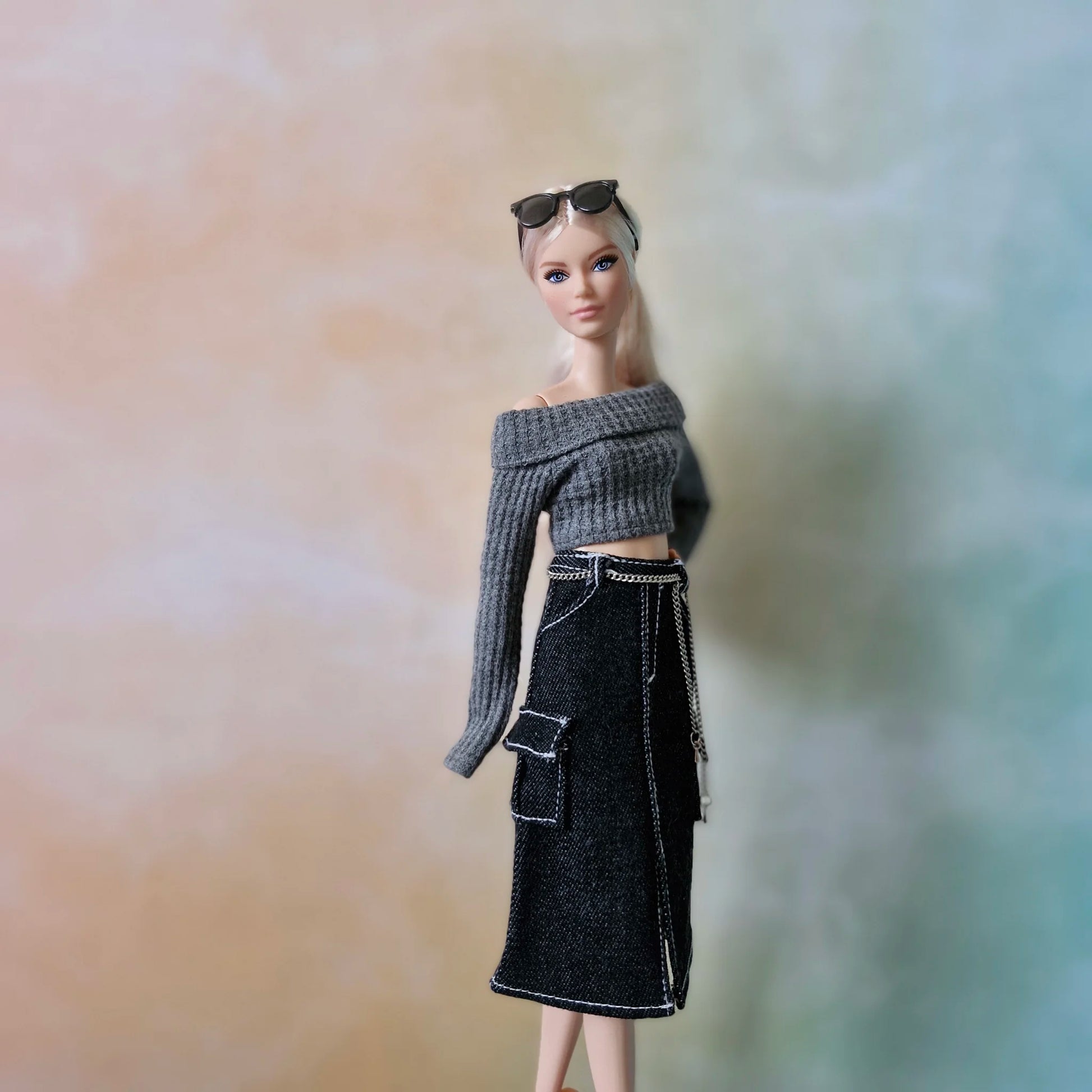 Fashion doll with sunglasses on head, wearing grey off-shoulder sweater and black denim midi skirt with cargo pockets.
