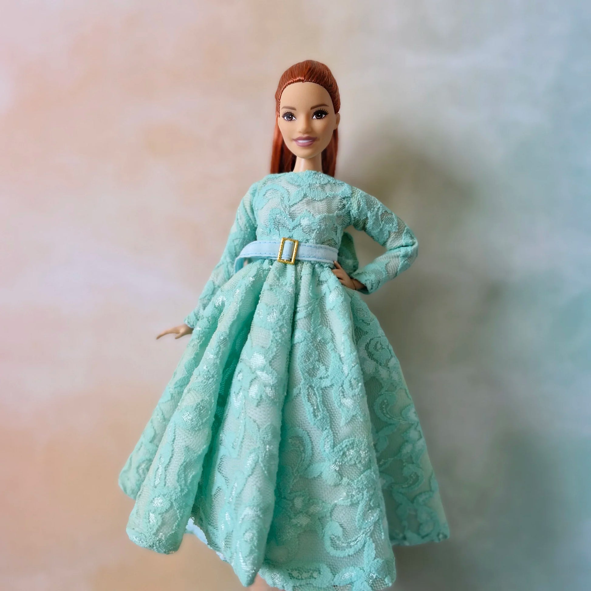 Barbie Curvy doll with red hair wearing elegant mint green long-sleeve lace dress with belt, posing with hand on hip.