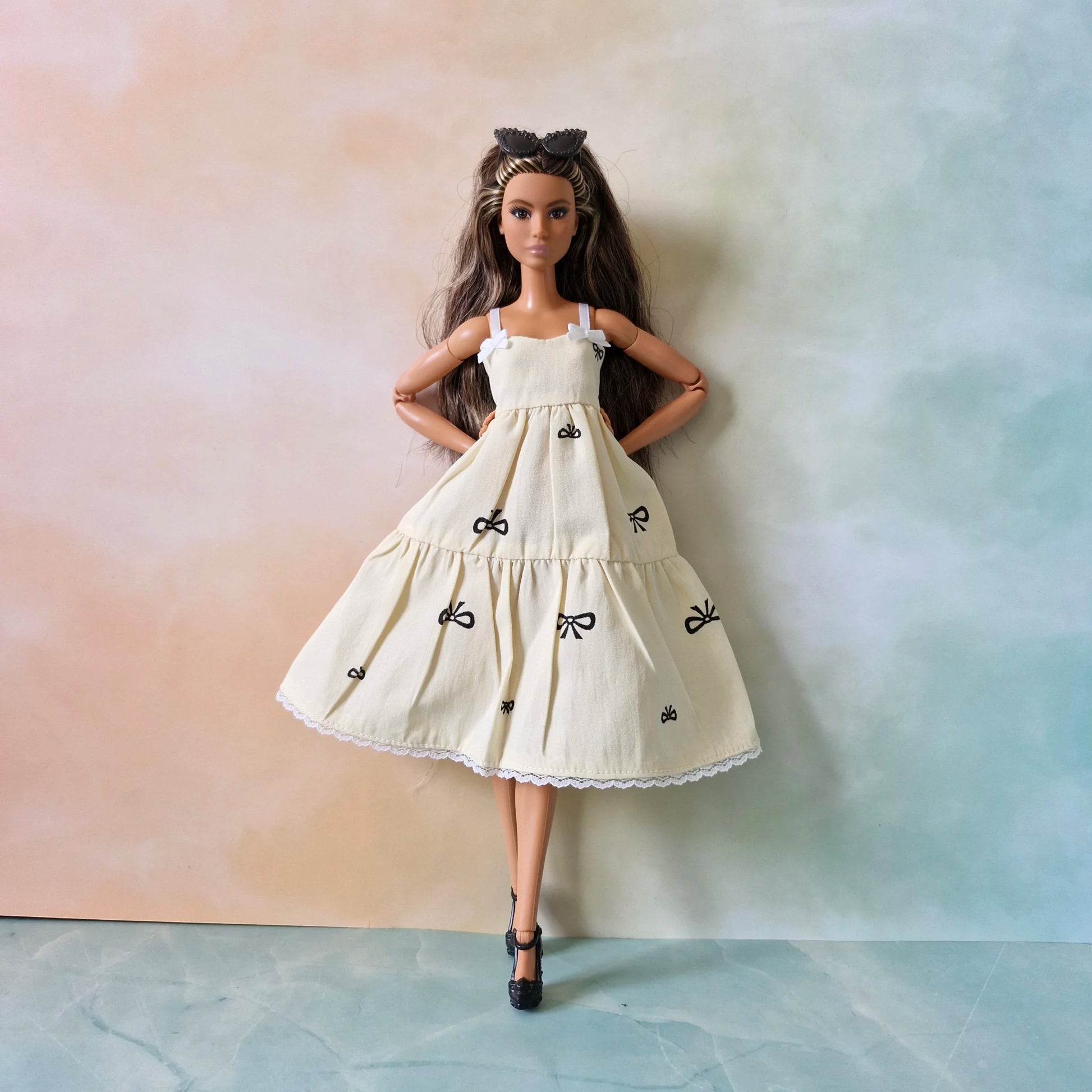 Brunette Barbie doll models cream bow print tiered sundress solo, sunglasses on head.