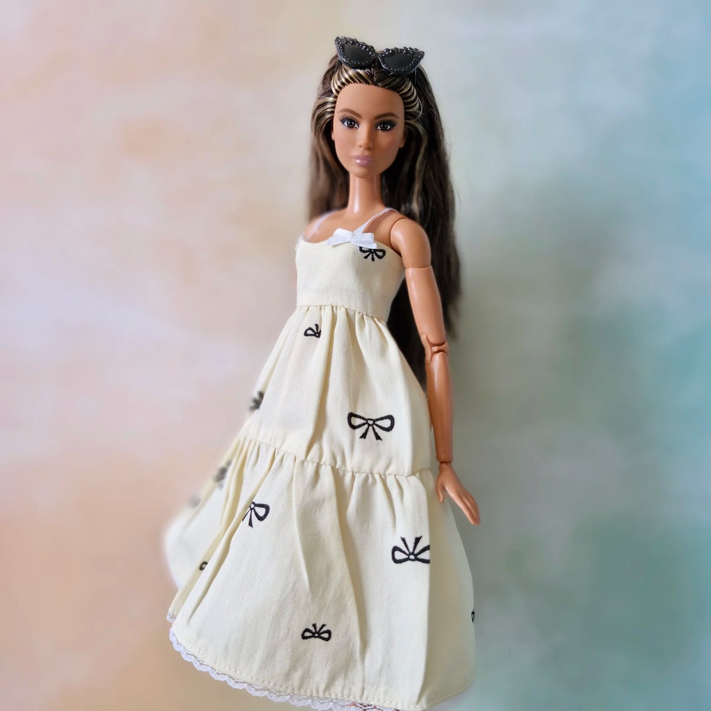 Brunette fashion doll wearing cream tiered sundress with black bow print and white lace hem.