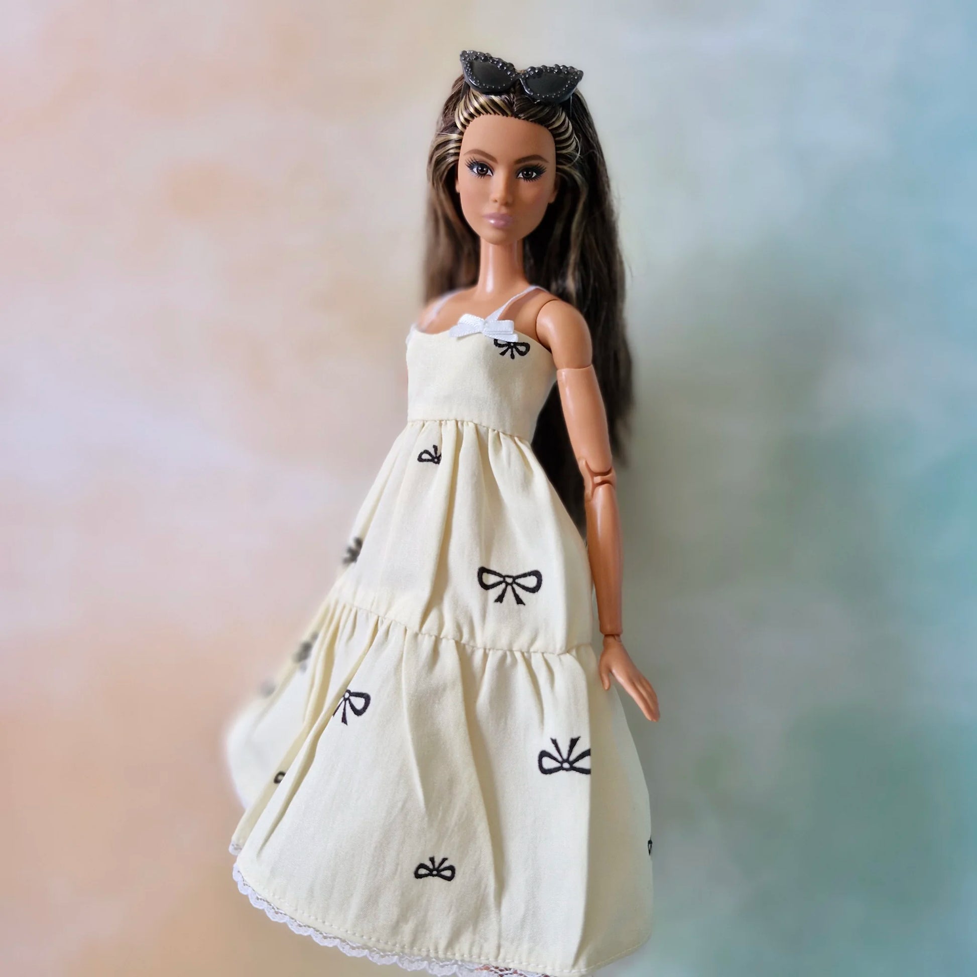 Brunette fashion doll wearing cream tiered sundress with black bow print and white lace hem.