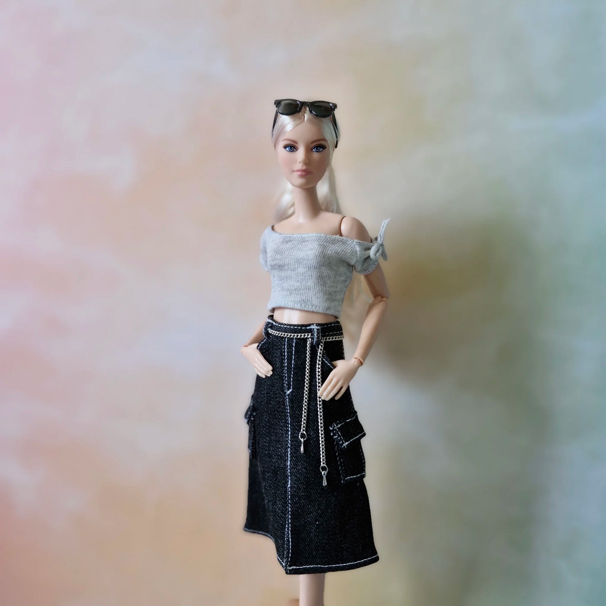 Full length view of blonde Barbie doll in grey top, black denim cargo skirt, and silver boots