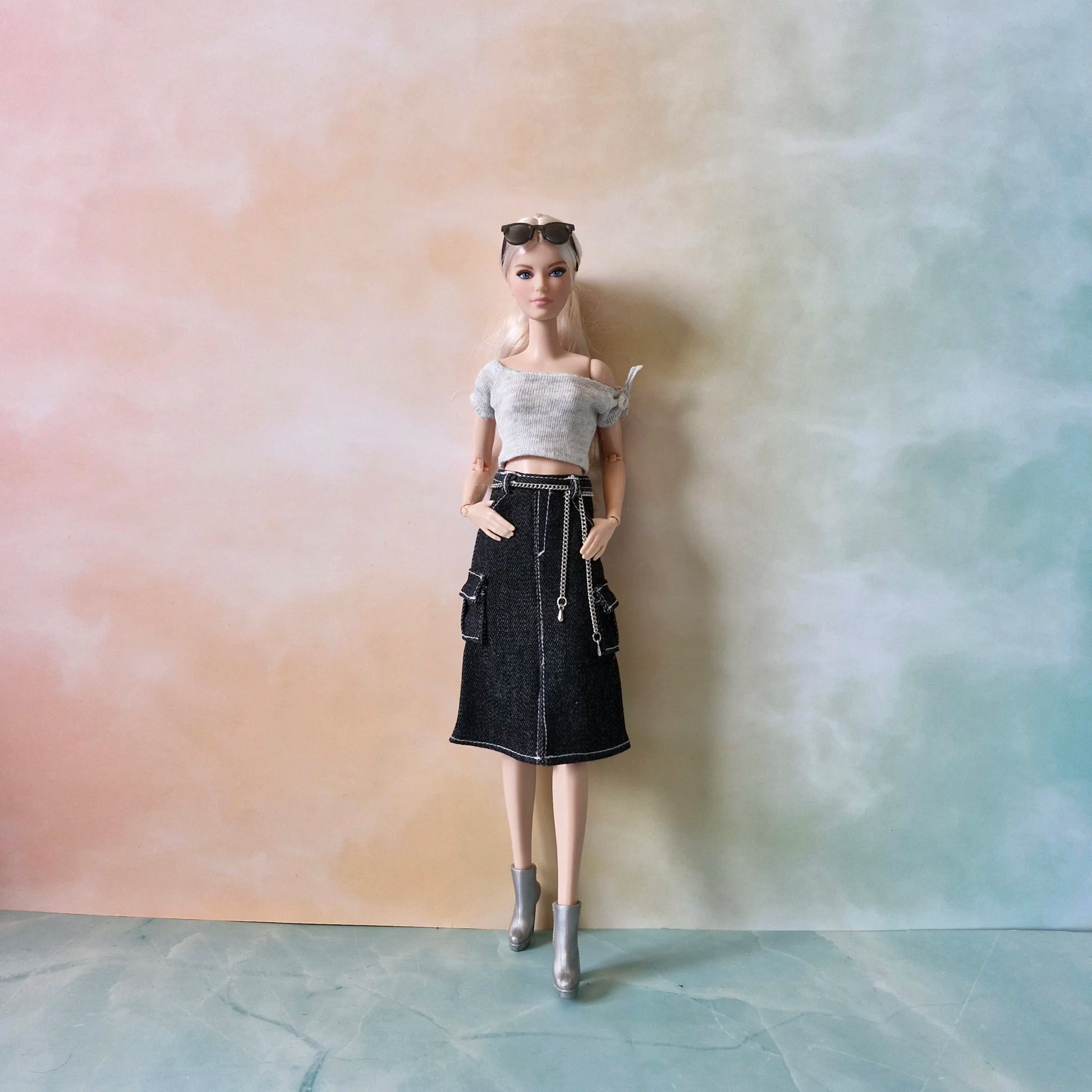 Blonde Barbie doll wears grey knit crop top and black denim cargo midi skirt, hands on hips