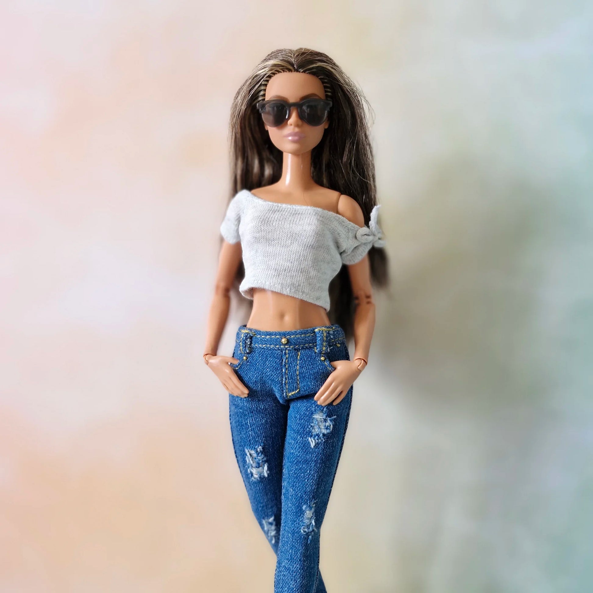 Brunette Barbie doll wearing white off-shoulder top and distressed blue skinny jeans with hands in pockets