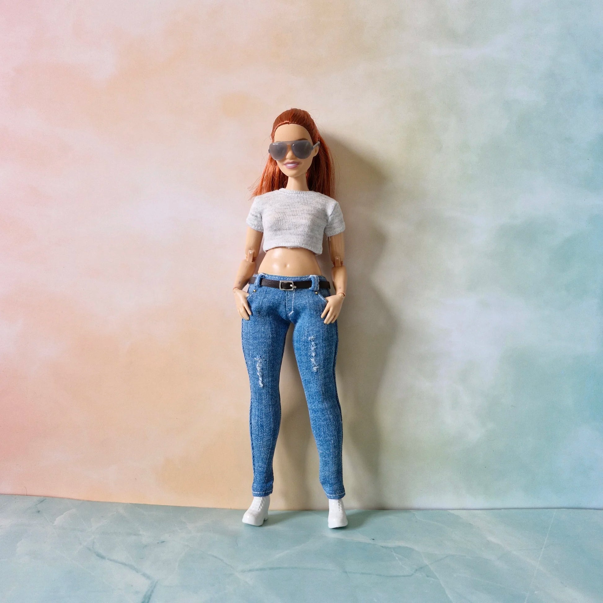 Redhead Barbie doll wearing grey crop top and distressed blue jeans with black belt and hands in pockets