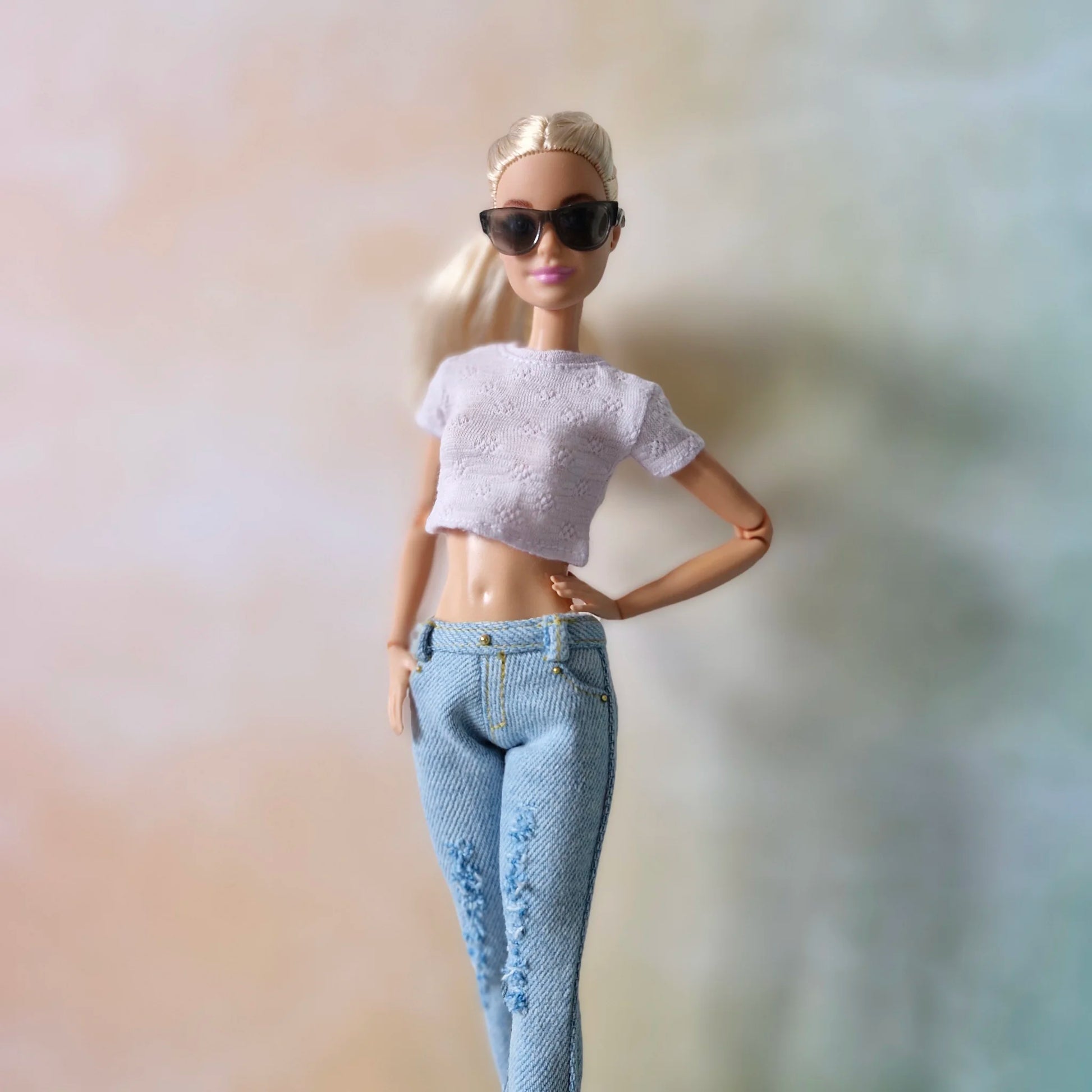 Blonde Barbie doll wearing white textured crop top and light blue distressed jeans with sunglasses