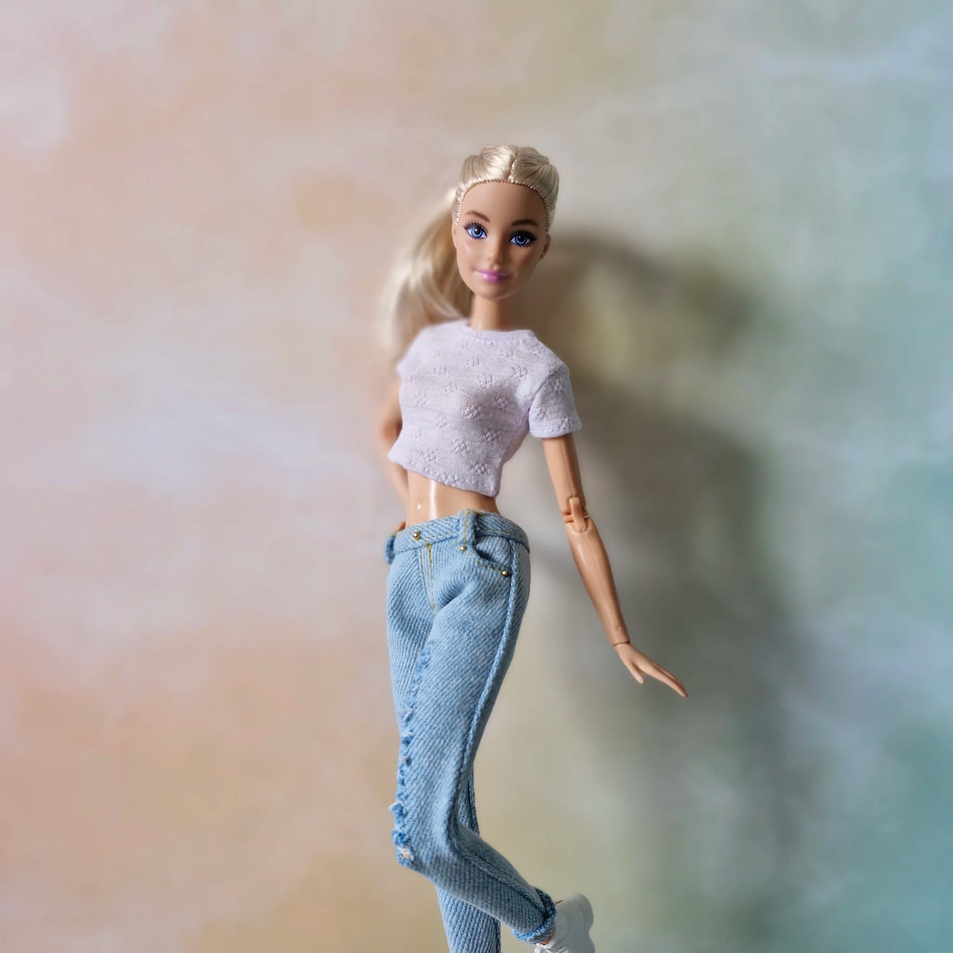 Blonde Barbie doll in white crop top and light blue ripped jeans kicking leg up