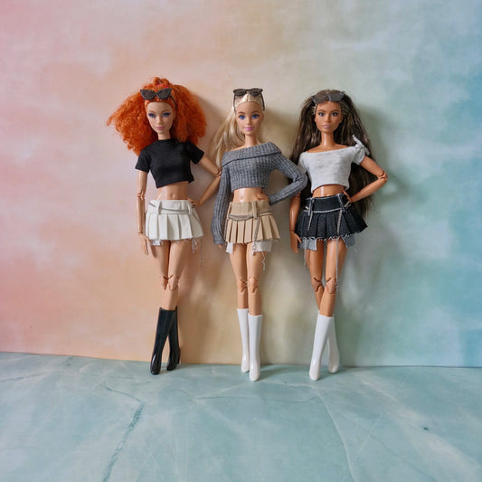Three fashion dolls showcasing pleated mini skirts with chain details and crop tops