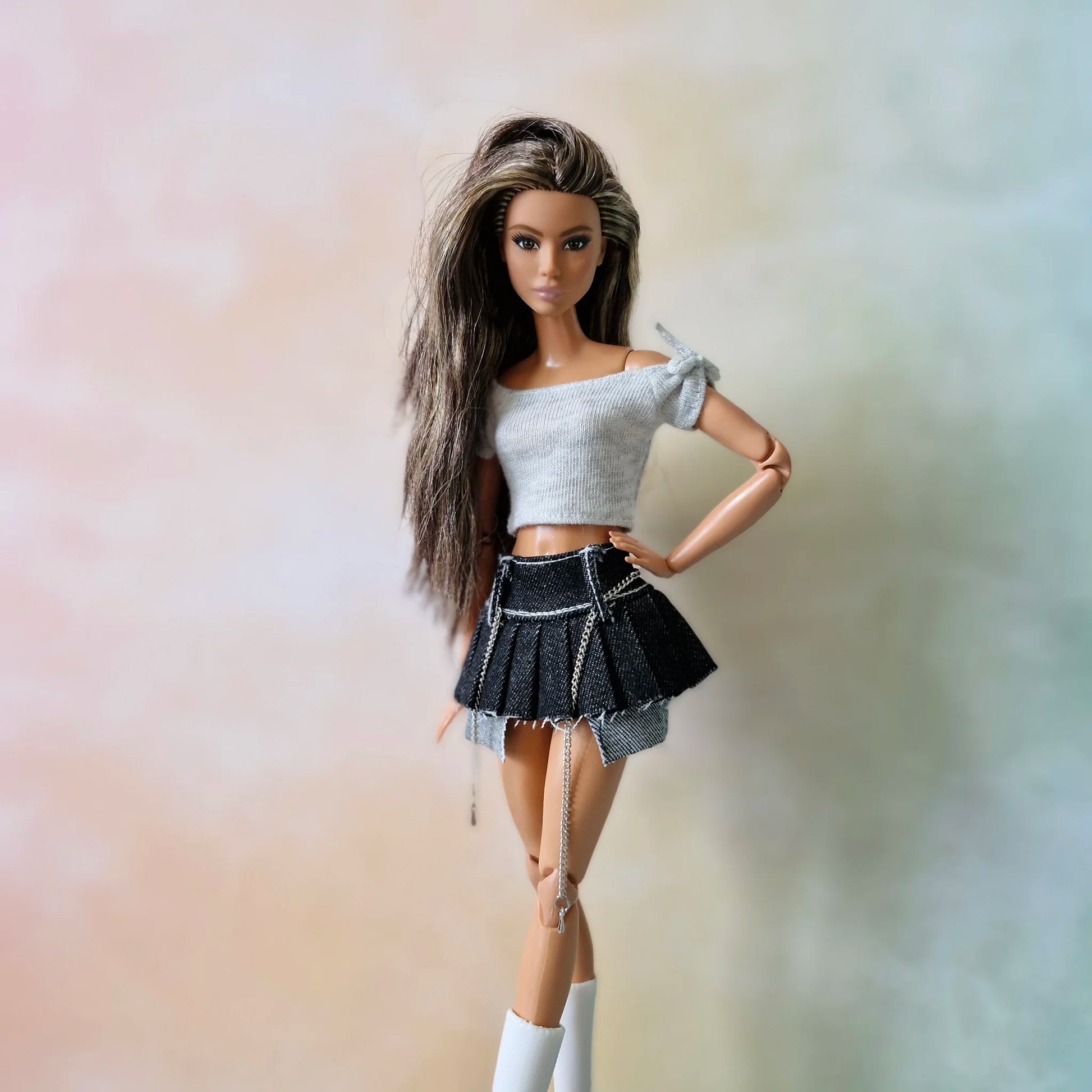 Brunette doll poses in white crop top and black denim pleated skirt with chain