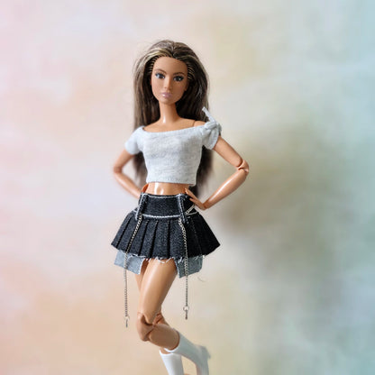 Brunette doll in white crop top and black denim pleated mini skirt with chain detail
