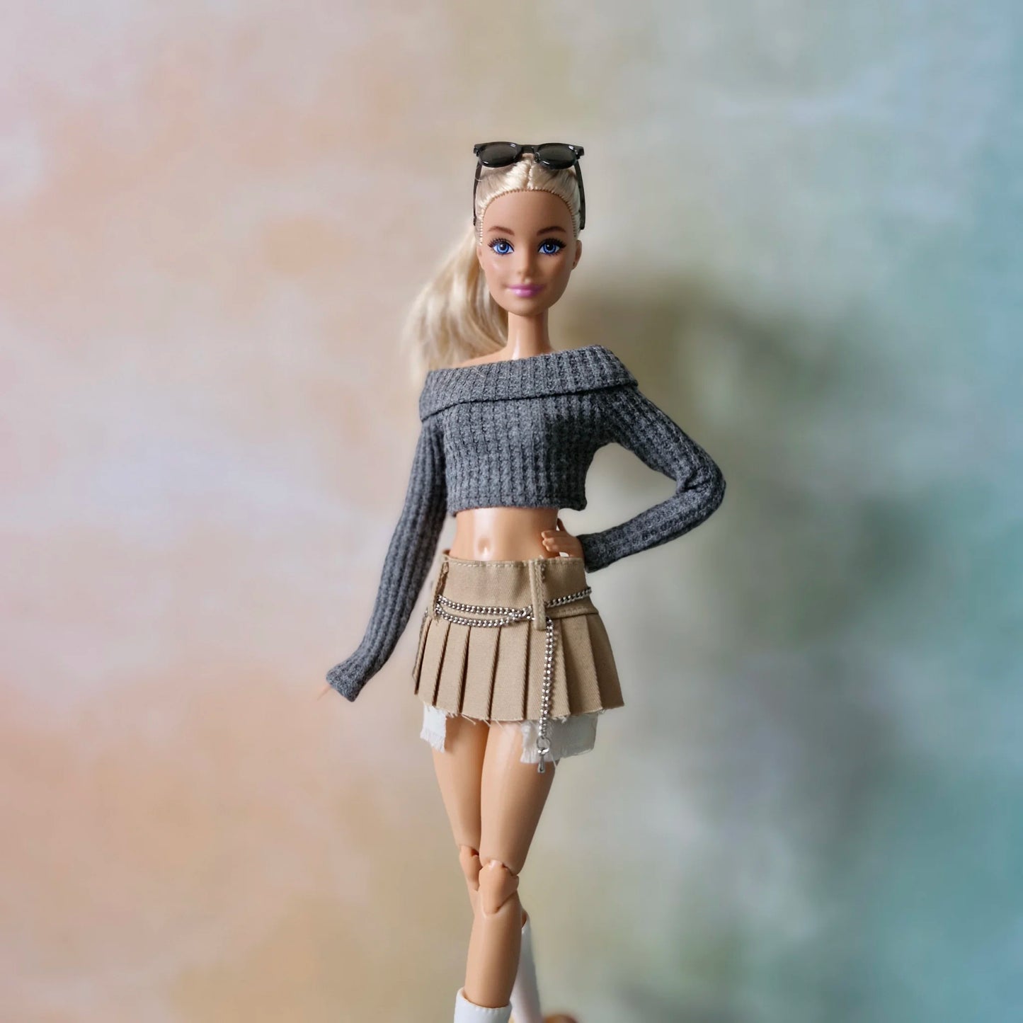 Blonde doll wearing grey off-shoulder crop top and khaki pleated mini skirt with chain detail