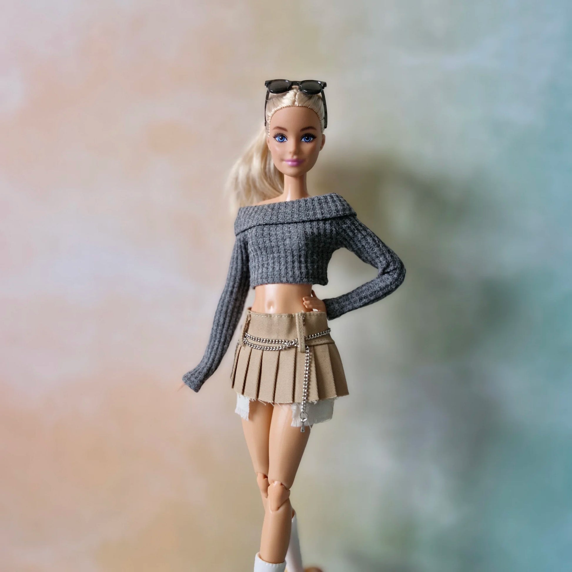 Blonde doll wearing grey off-shoulder crop top and khaki pleated mini skirt with chain detail