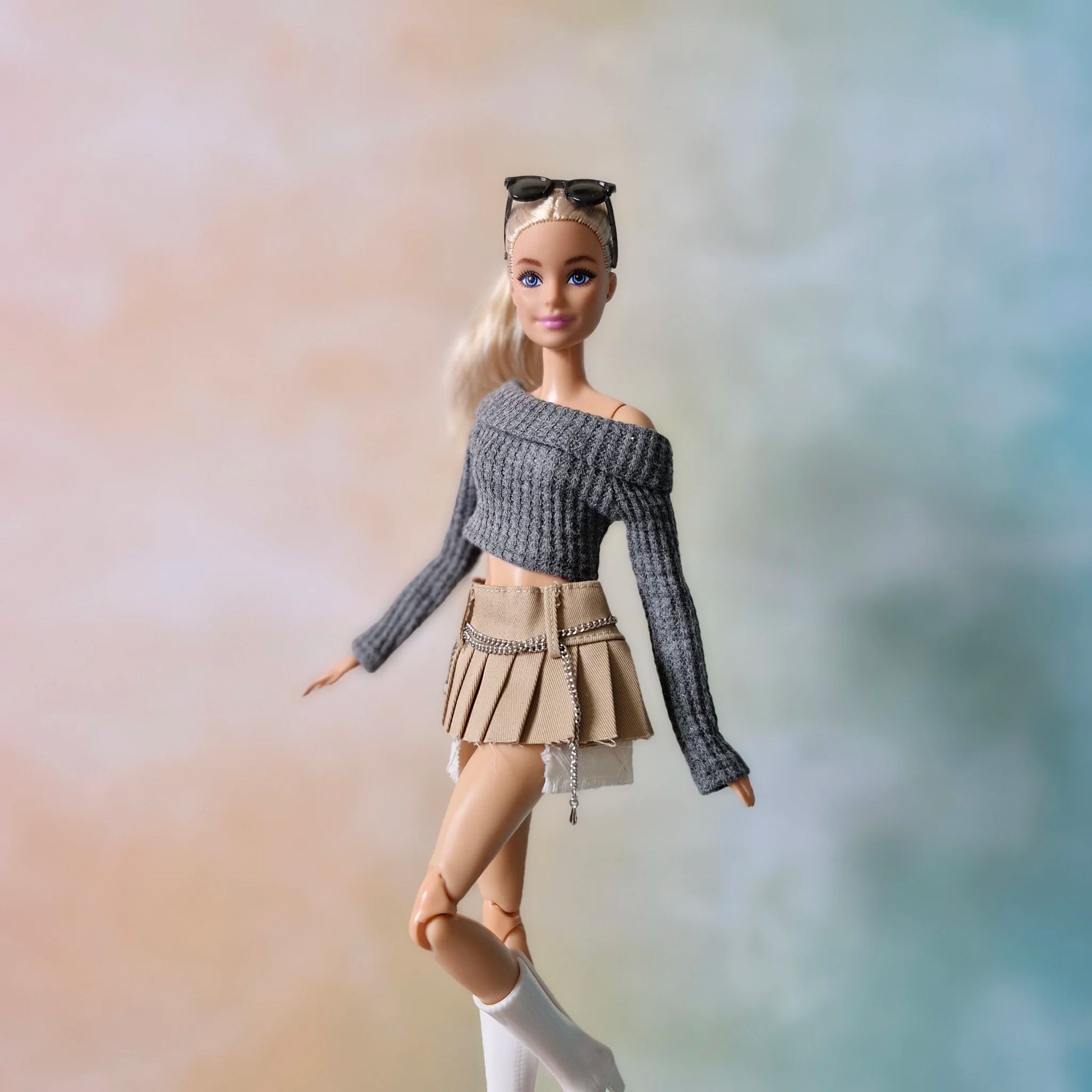 Blonde doll modeling grey crop top and khaki pleated chain skirt outfit in walking pose