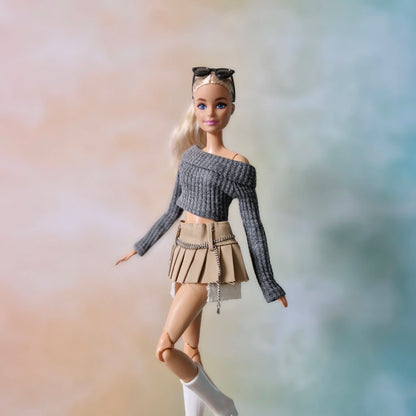 Blonde doll modeling grey crop top and khaki pleated chain skirt outfit in walking pose