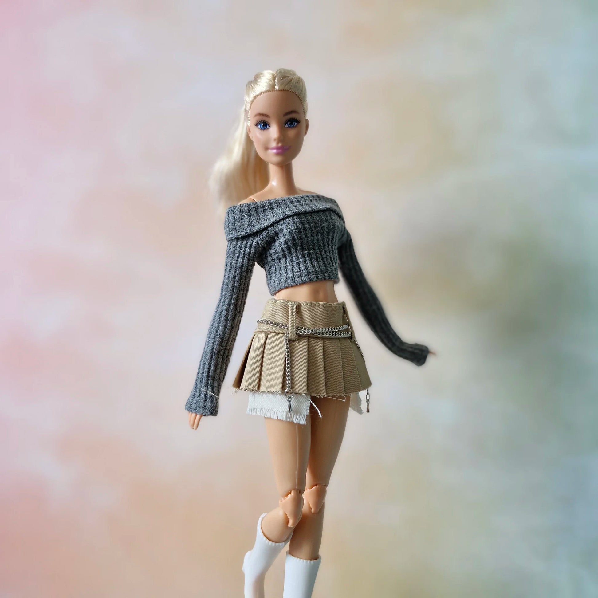 Fashion doll wearing grey knit crop top and khaki pleated skirt with chain and boots
