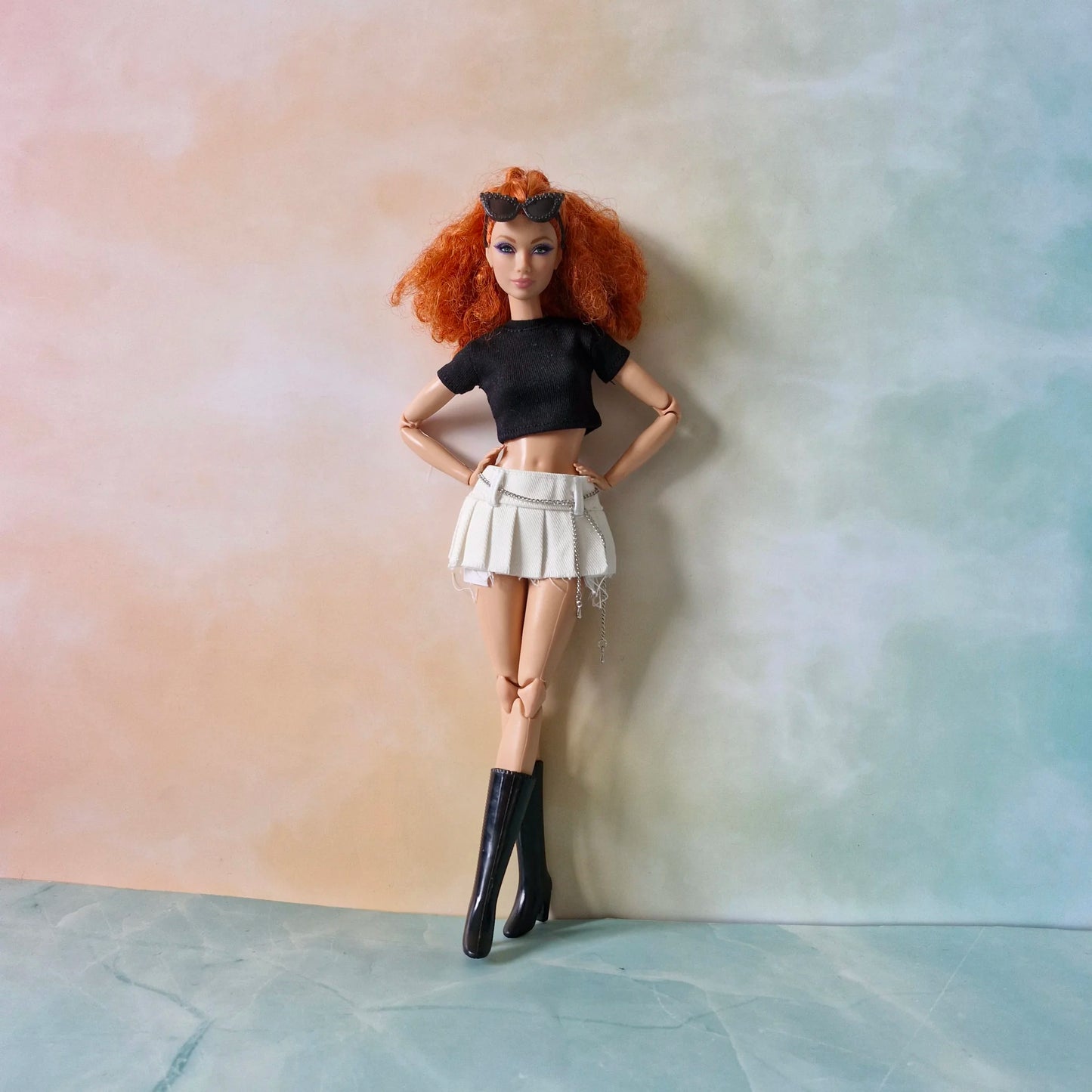 Full view redhead doll in black crop top, white pleated chain skirt, and black boots