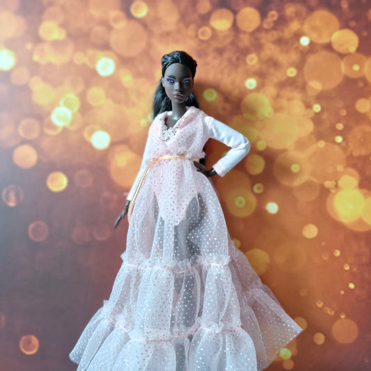 Dark-skinned Barbie doll models elegant pink tiered sparkly tulle gown with gold belt, bokeh background.