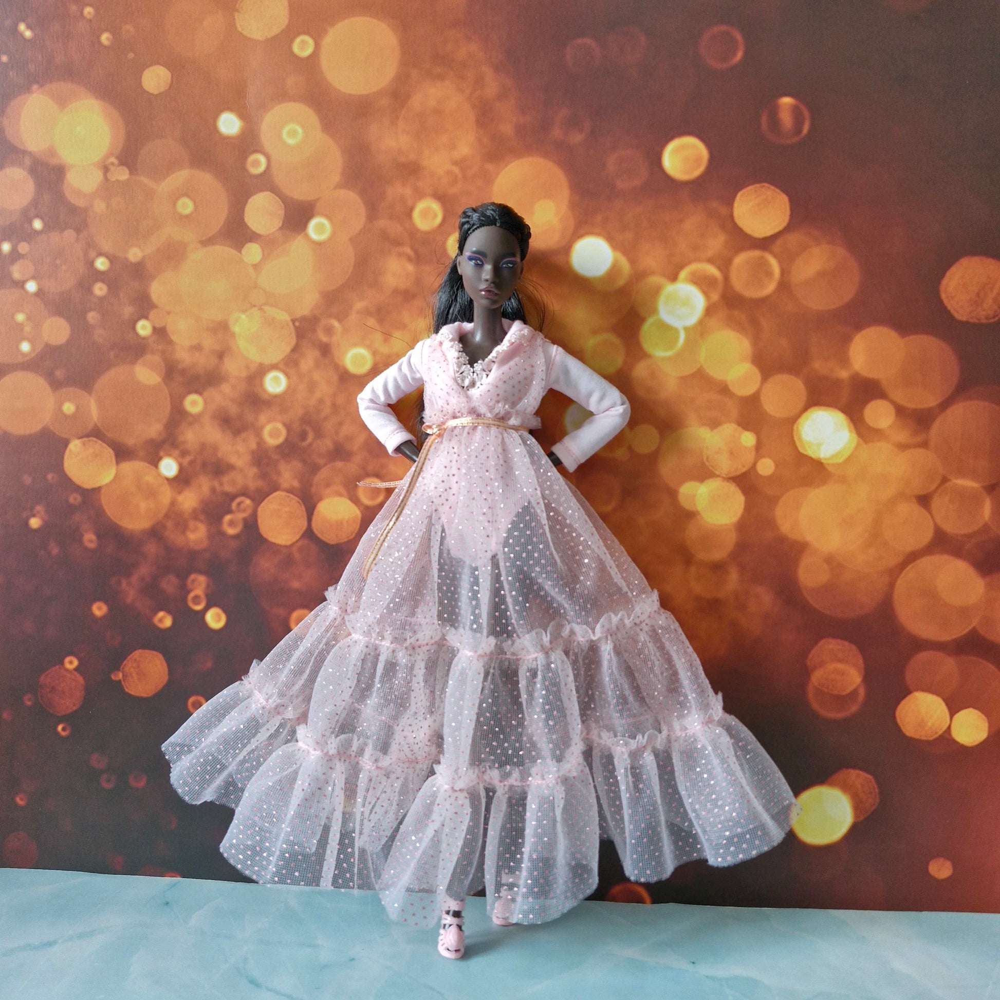 Full view of dark-skinned Barbie doll wearing elegant pink tiered sparkly tulle gown with gold belt.